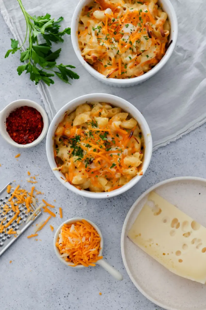 Tres bowls de mac and cheese vistos desde arriba con queso rallado y rallador