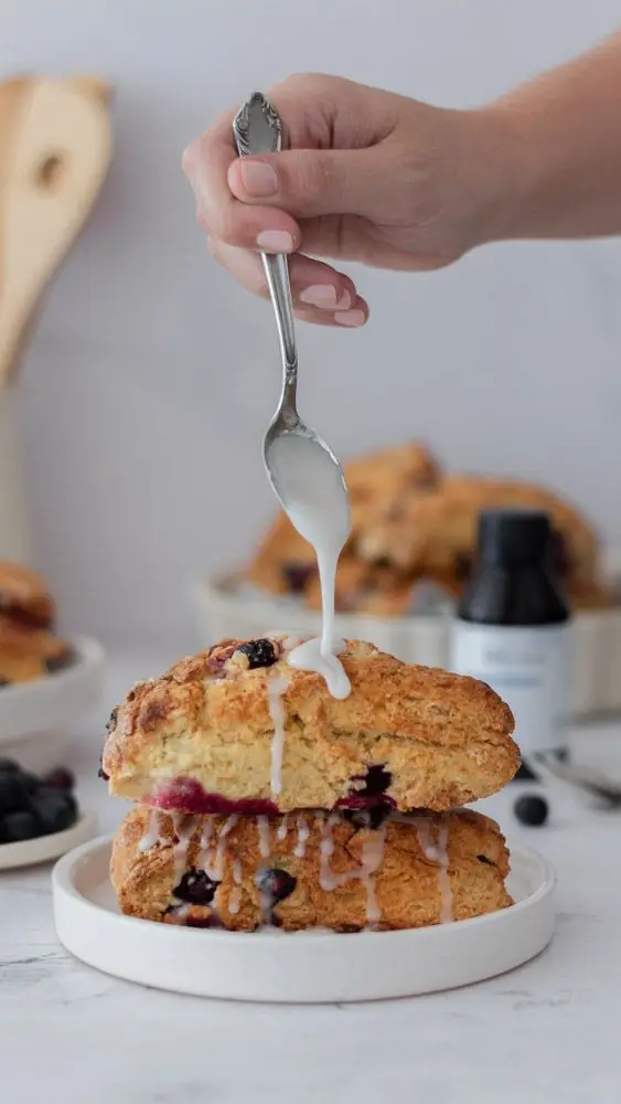 Scone de arándanos con glaseado cayendo desde una cuchara