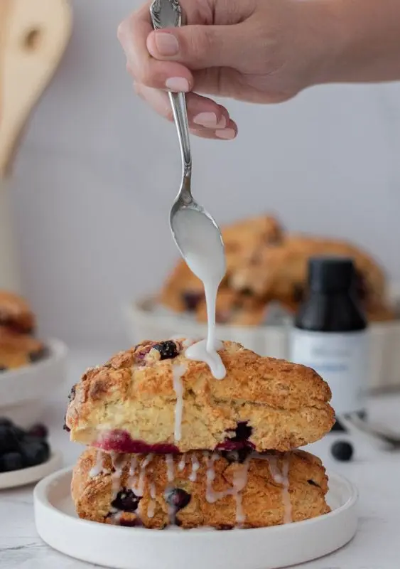 Scone de arándanos con glaseado cayendo desde una cuchara